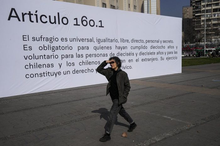 Persona frente a cartel con artículo de la Constitución rechazada en Chile